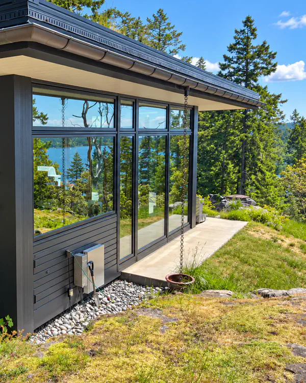 A wall of clean windows on a house above the water, with trees and blue sky.