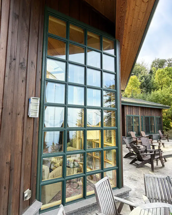 A tall window of many small panes on a wood-sided house, next to a patio.
